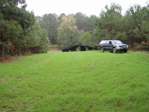 1995 Ford Bronco - A dark SUV with a camper shell is parked in a grassy field with trees and a barn in the background.