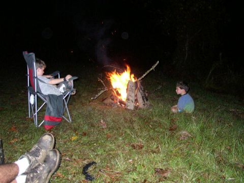 1995 Ford Bronco - A nighttime campfire scene with two children and a person's legs visible in the foreground.