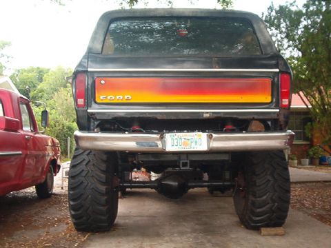 1979 Ford Bronco - Rear view of a lifted 1979 Ford Bronco with custom paint on the tailgate, next to a red truck.