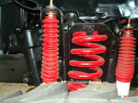 1979 Ford Bronco - Close-up of red suspension components, including a coil spring and shock absorber with protective bellows.