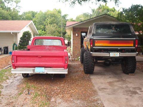 1979 Ford Bronco - A lifted 1979 Ford Bronco with a distinctive tailgate stripe sits in a driveway next to a red pickup truck.