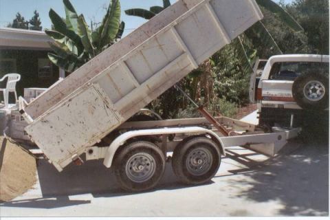 1990 Ford Bronco - A dump trailer is raised next to a white SUV with a spare tire on the back.