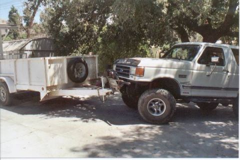 1990 Ford Bronco - A lifted white Ford Bronco is hitched to a white utility trailer in a driveway.