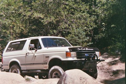 1990 Ford Bronco - This 1990 Ford Bronco is shown off-roading on a rocky trail with trees in the background.