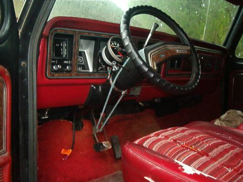 1979 Ford Bronco - The interior of the vehicle shows red upholstery and dashboard details, with the steering wheel and pedals in view.