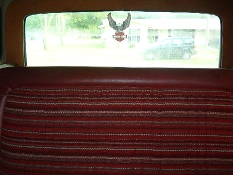 1979 Ford Bronco - View from inside a vehicle's rear seat, looking out the back window at a house and another car.