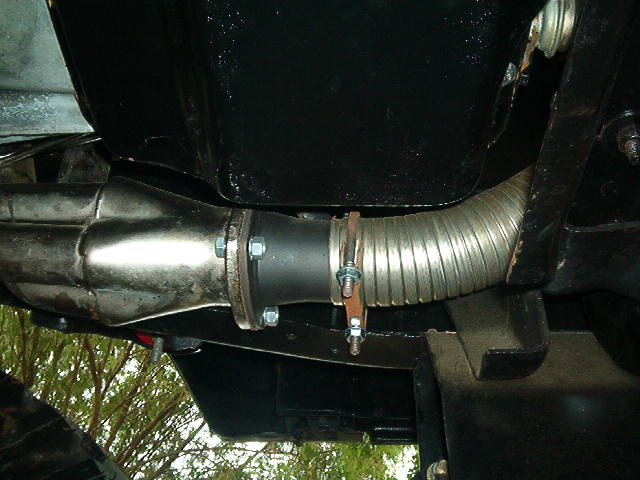 Exhaust pipe connection with flexible metal tubing and bolted flange. Black undercarriage visible