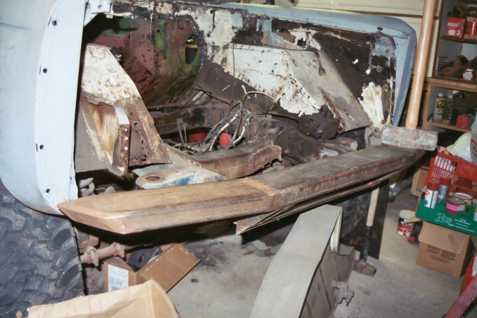 rusted vehicle chassis with front end removed, showing frame and engine bay components