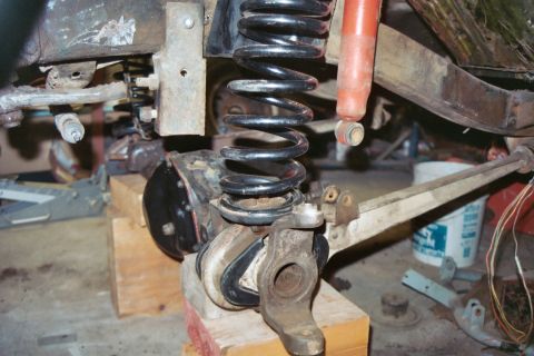 1966 Ford Bronco - Close-up of vehicle suspension parts, including a coil spring and shock absorber, undergoing work.