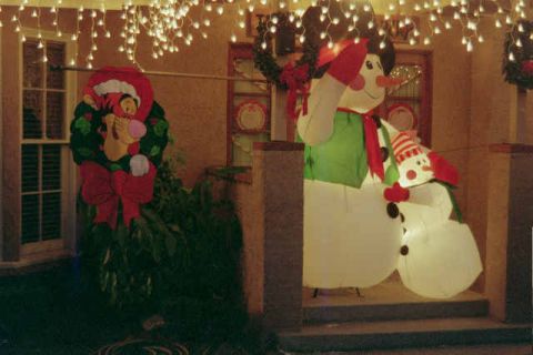1988 Ford Bronco - Christmas decorations including inflatable snowmen and a Tigger wreath adorn a porch under twinkling lights.