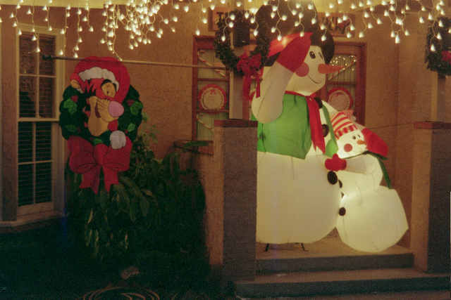 inflatable snowmen and a Tigger wreath on a porch with Christmas lights