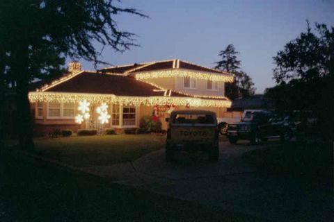 1988 Ford Bronco - Two trucks are parked in the driveway of a house adorned with festive holiday lights.