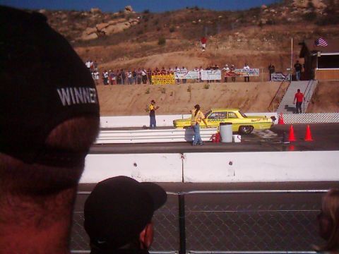 1978 Ford Bronco - A yellow sedan is staged on a drag strip with spectators in the background.