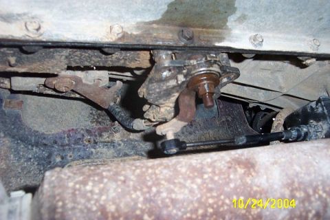 1988 Ford Bronco - Close-up view of rusty undercarriage components, including a mechanical linkage and exhaust system.