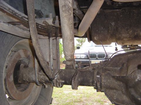 1993 Ford Bronco - Undercarriage view of rear axle and suspension parts, with a car in the background.