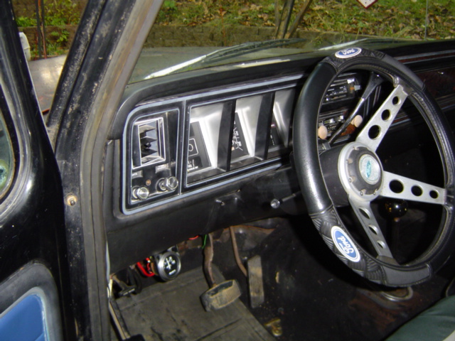 Dashboard and steering wheel of a 1979 Ford Bronco, showing a black dashboard with rectangular gauges and a silver steering wheel with a Ford logo