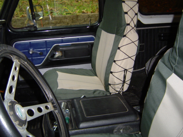 Interior view of vehicle with green and tan seat covers, aftermarket steering wheel, and center console