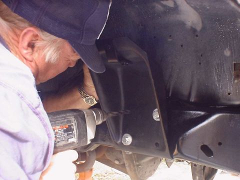 1988 Ford Bronco - A person is drilling a hole into the black metal frame of a vehicle, focusing on the task.