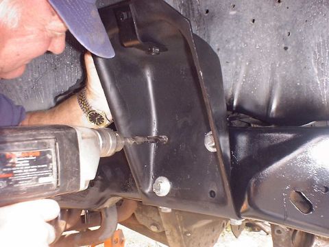 1988 Ford Bronco - A person drills into a black metal bracket attached to the vehicle's front axle assembly.