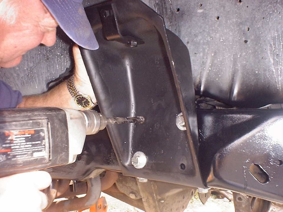 Drilling into black metal bracket on vehicle's front axle assembly