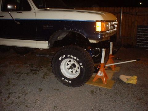 1988 Ford Bronco - The front of a lifted Ford Bronco is supported by jack stands, with a close-up of the front axle and tire.