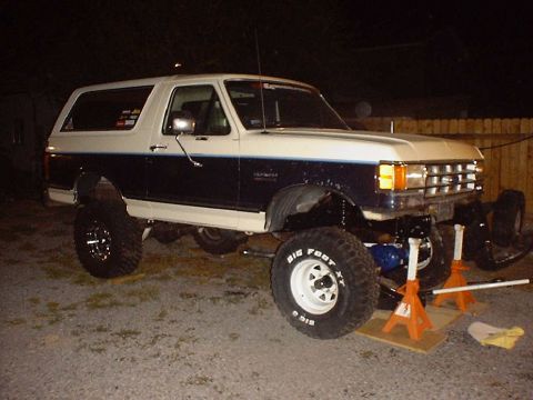 1988 Ford Bronco - A lifted two-tone blue and white Ford Bronco is shown with its front axle removed and supported by jack stands.