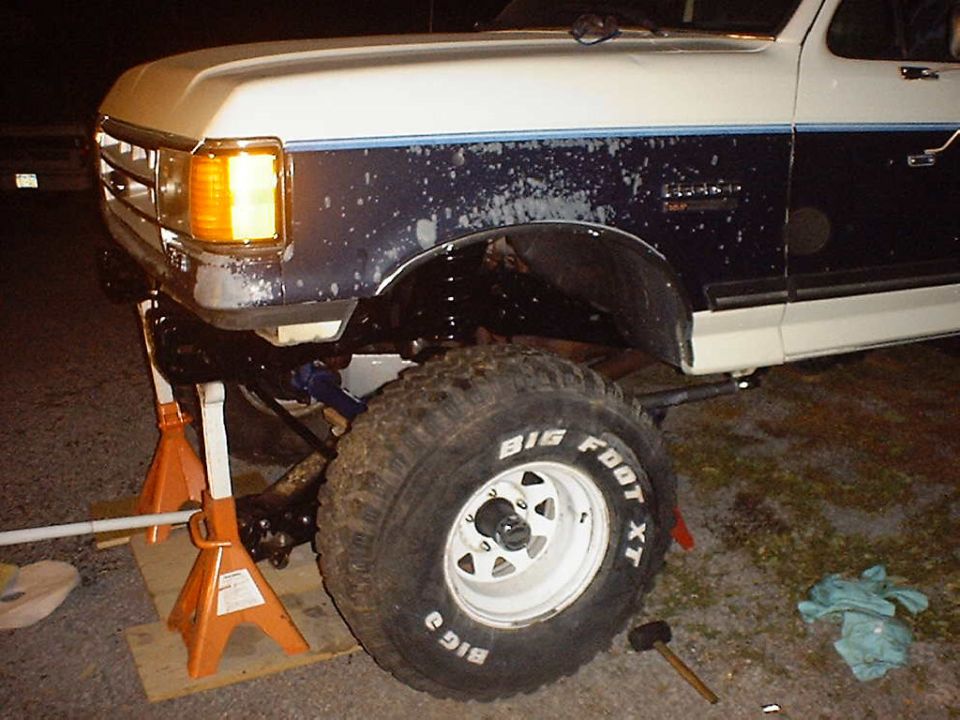 Front axle and Big Foot XT tire on a lifted truck, supported by jack stands