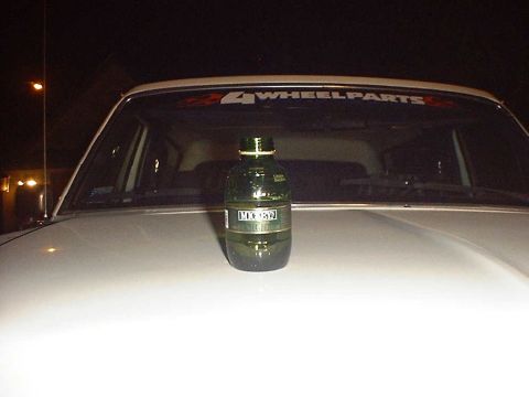1988 Ford Bronco - Bottle of fluid sits on the hood of a vehicle with a '4 WHEELPARTS' sticker.
