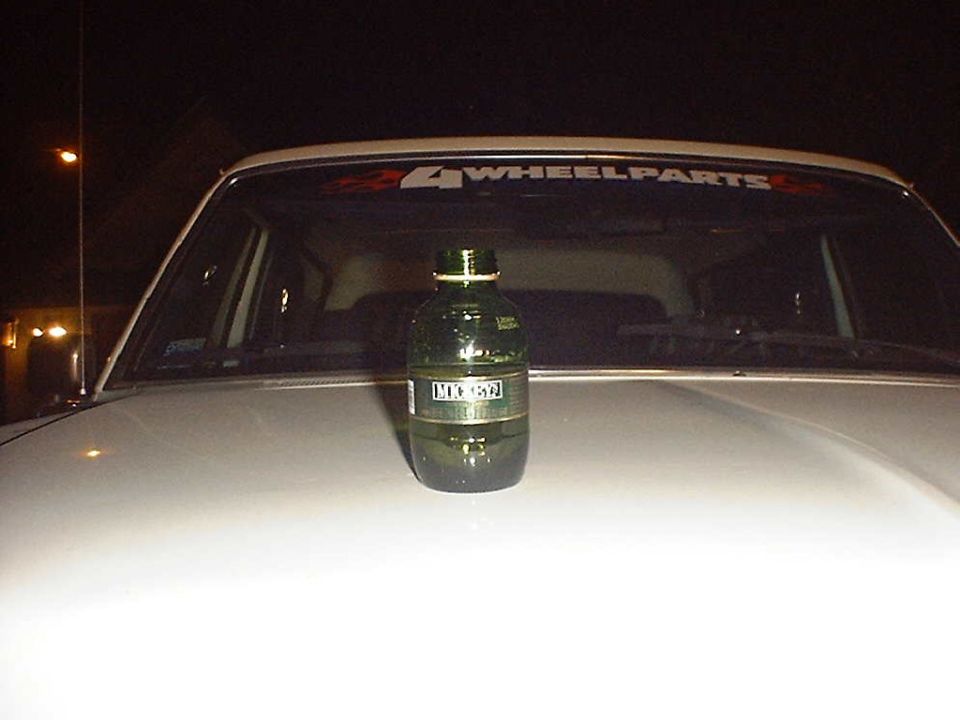 Green bottle on white car hood with '4 WHEELPARTS' sticker on windshield
