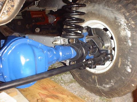 1988 Ford Bronco - Close-up view of a vehicle's front axle assembly, painted blue, with a black shock absorber and tire.