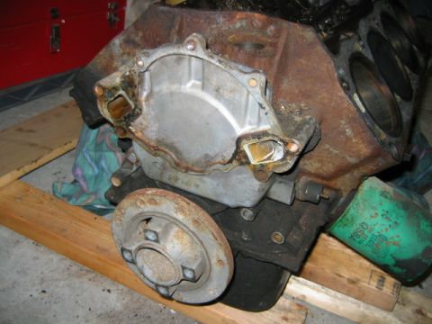 1992 Ford Bronco - Rear view of an engine block resting on a wooden pallet, showing the bare bellhousing area with a bolted-on flywheel/flexplate cover and ru…