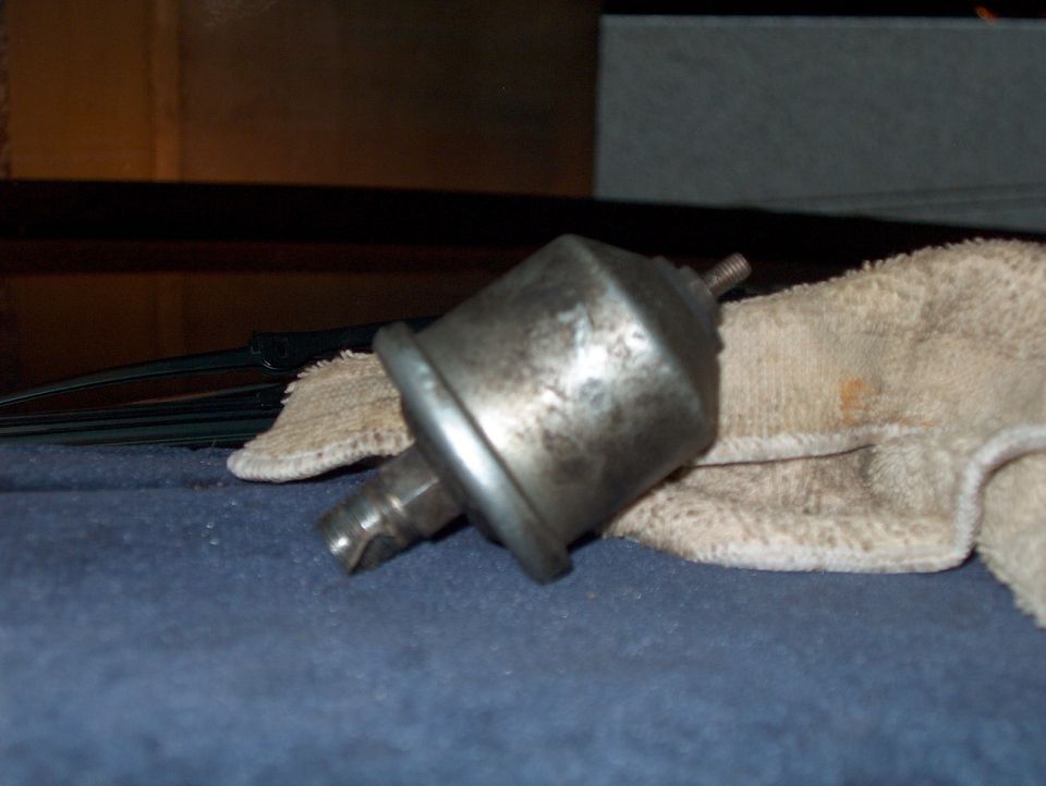 Metal automotive part with threaded stud and hose connection, resting on a cloth
