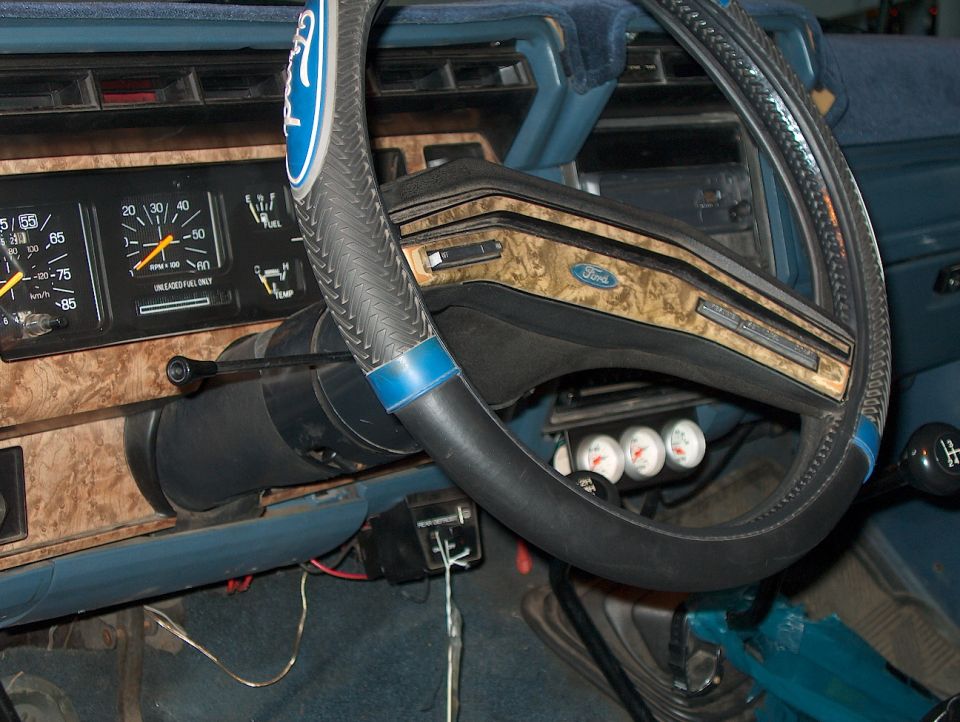 Ford truck dash with woodgrain cluster, laced steering wheel cover and three aftermarket gauges