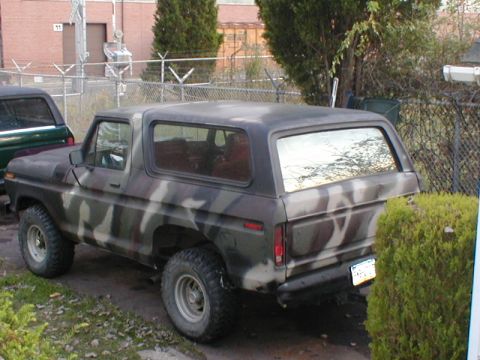 1979 Ford Bronco - This camouflaged SUV is parked outdoors next to another vehicle.