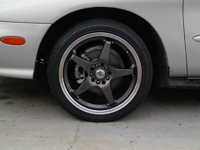 Silver car's front wheel with custom dark grey five-spoke rims and a red side marker light