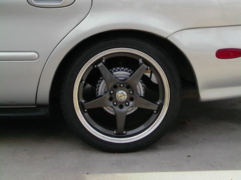 1999 Ford Taurus - The rear wheel and fender of a silver 1999 Ford Taurus, a custom five-spoke wheel with a dark gray finish and chrome lip.