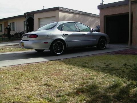 1999 Ford Taurus - A silver sedan with black rims is parked in a driveway next to a garage.