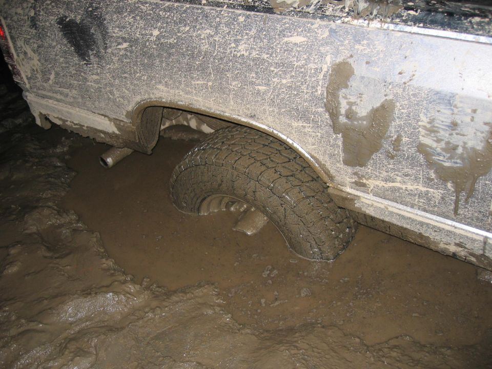 Muddy tire sunk deep in thick mud next to a dirty vehicle body