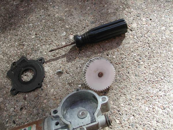 Car window motor parts including a gear, housing, and black plastic piece on concrete