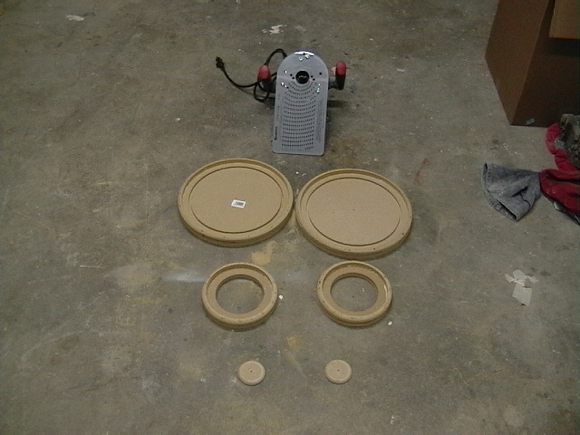 Router and four wooden speaker mounting rings on a concrete floor