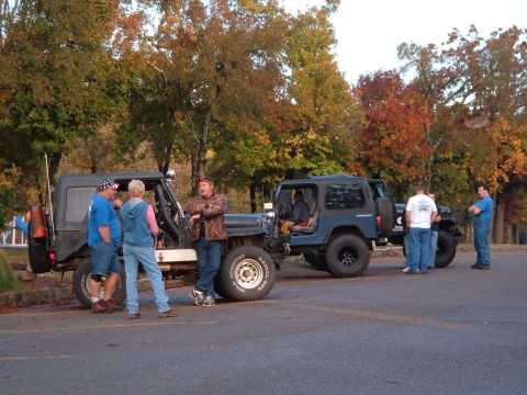 1986 Ford Bronco - People gather around two Jeeps in a parking lot during autumn.