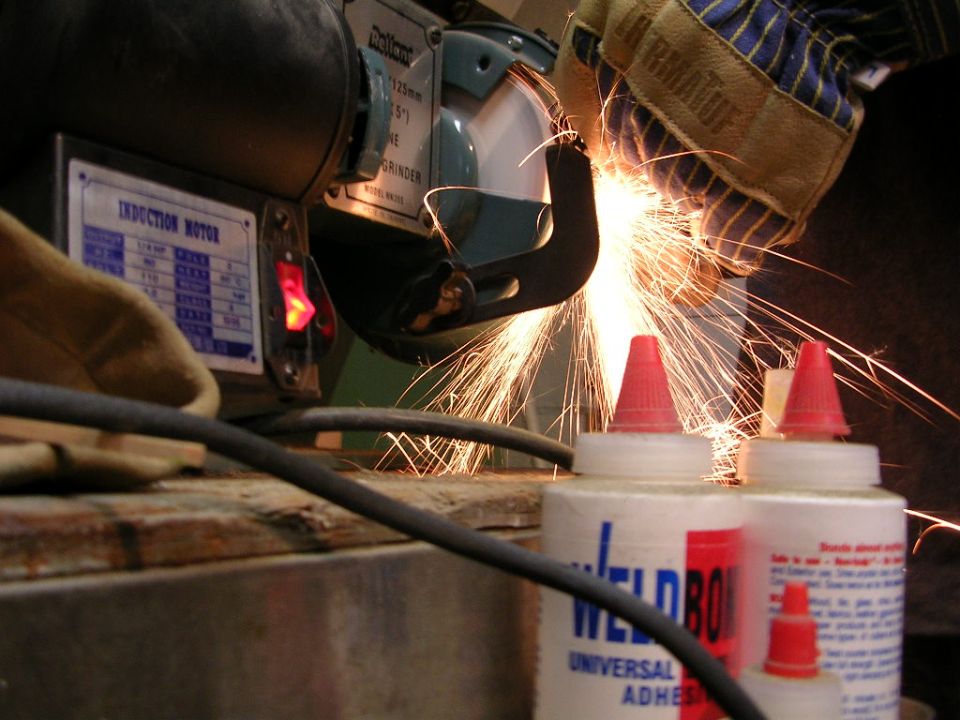Bench grinder in use, creating sparks. Two bottles of Weld-On adhesive are in the foreground