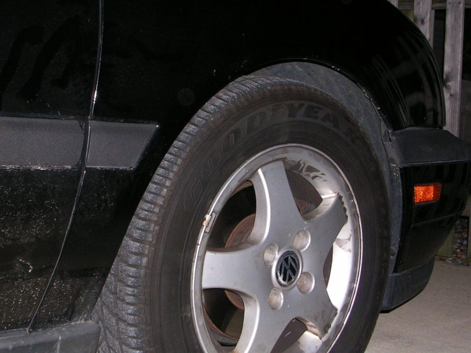 Black car's front wheel with a silver five-spoke rim and a Goodyear tire. The body has a black trim strip