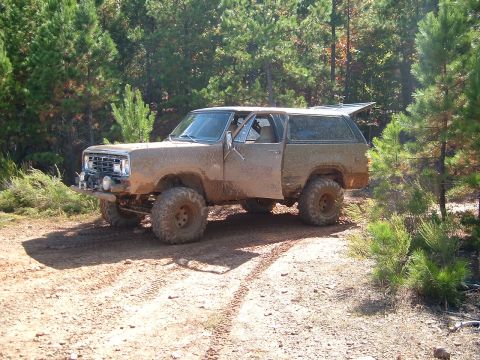 1986 Ford Bronco - This heavily modified SUV, covered in mud, navigates a rough dirt path through a wooded area.