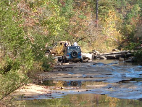 1986 Ford Bronco - Off-roading Jeeps navigate a shallow, rocky stream during autumn.