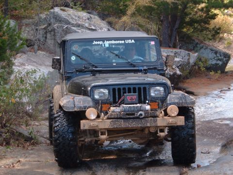 1986 Ford Bronco - A black Jeep Wrangler navigates a muddy, rocky path during an off-road event.