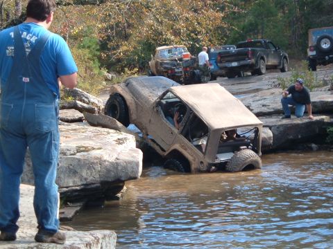 1986 Ford Bronco - Several off-road vehicles are navigating a challenging rocky terrain with water obstacles.