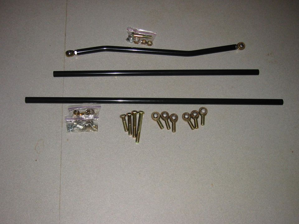 Suspension link kit with bent track bar, two black tubular bars, heim joints, and bolts on floor