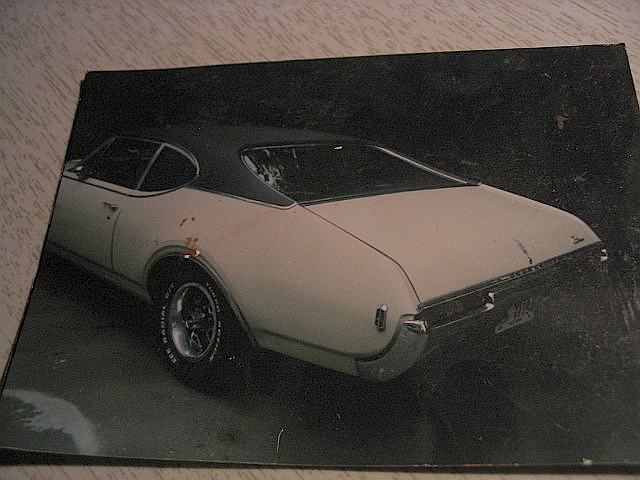 Rear 3/4 view of a white 1969 Oldsmobile 442 coupe with a black vinyl top