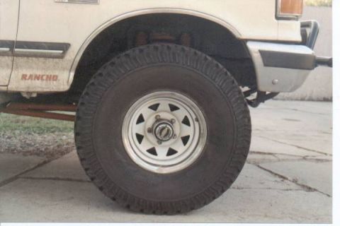 1990 Ford Bronco - Close-up of a white SUV's front wheel and fender, showing a "Rancho" decal.